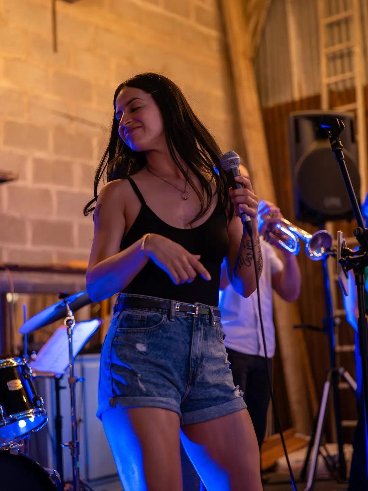 Alejandra danse sur scène sous la lumière bleue, un trompettiste derrière elle